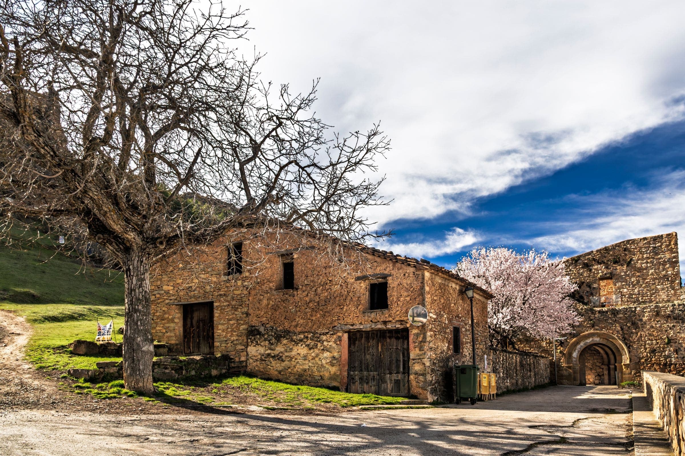 Casa de pedra amb un ametller florit al costat d'un camí de terra