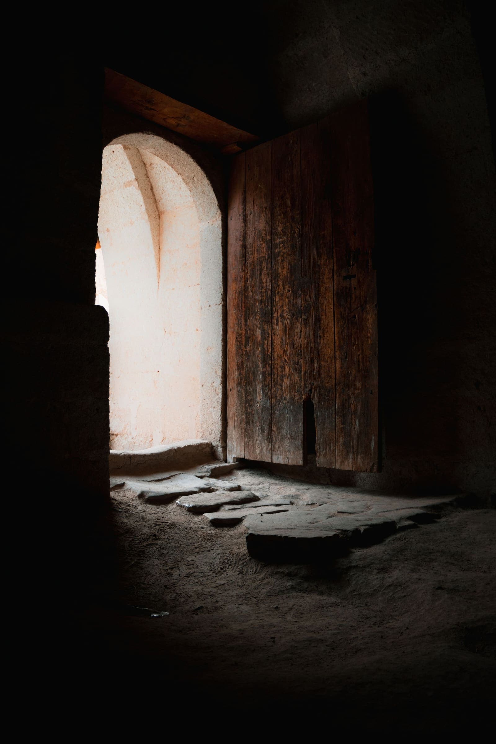 Porta de fusta oberta en un mur gruixut de pedra, amb llum natural que entra a l'interior